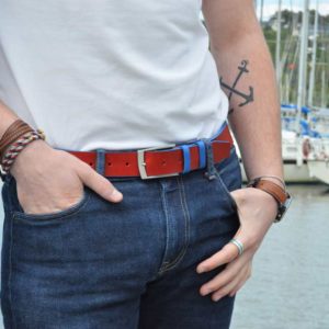 ceinture en cuir bicolore rouge et bleu porté sur un jean brut devant des bateaux